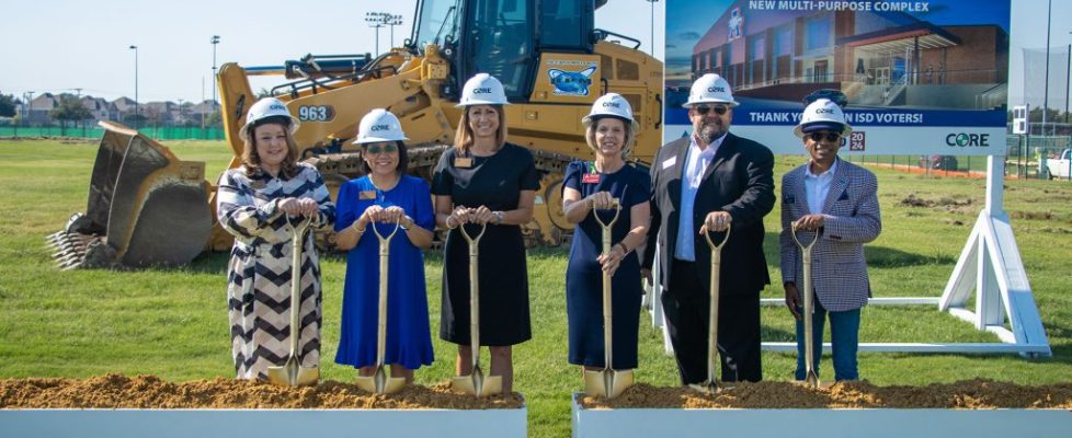 Six people in CORE construction helmets stand with gold shovels at a groundbreaking site in front of a sign for a new activity and multi-purpose complex.