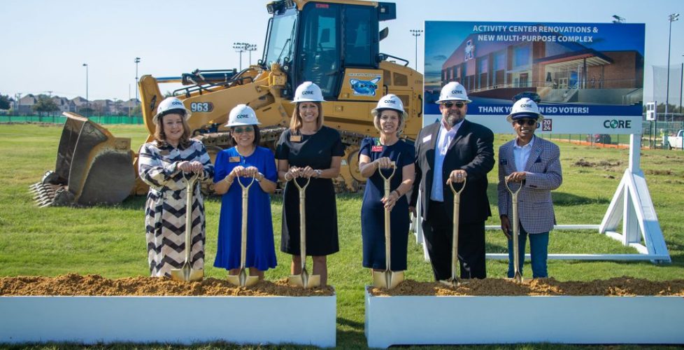 Six people in CORE construction helmets stand with gold shovels at a groundbreaking site in front of a sign for a new activity and multi-purpose complex.