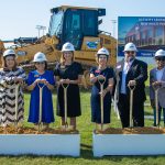 Six people in CORE construction helmets stand with gold shovels at a groundbreaking site in front of a sign for a new activity and multi-purpose complex.