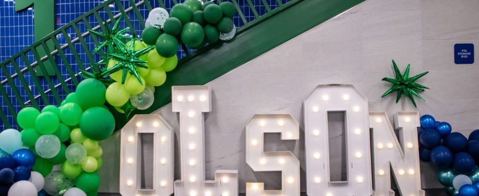 Light-up “OLSON” letters with green and blue balloon decorations arranged under a staircase.
