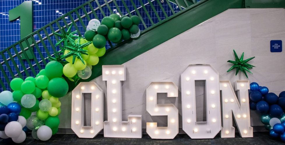 Light-up “OLSON” letters with green and blue balloon decorations arranged under a staircase.