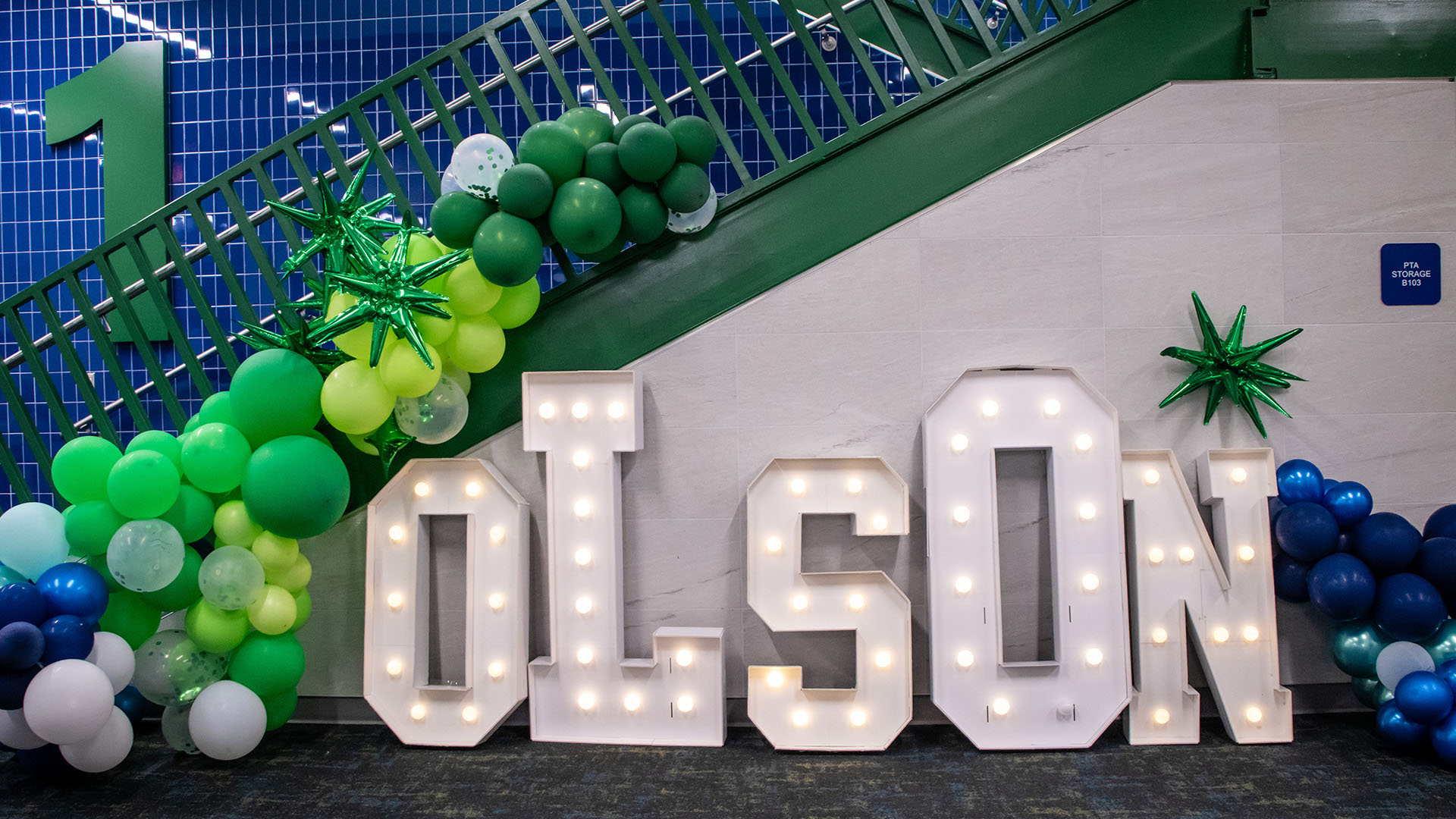 Light-up “OLSON” letters with green and blue balloon decorations arranged under a staircase.